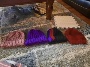 Four crochet hats in the colors, pink, purple, black, and red