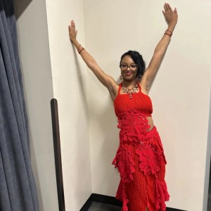 A girl with a red, crochet two-piece dress with both hands on the walls
